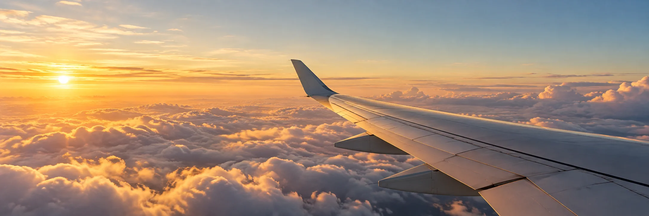 An airplane wing above sunlit clouds